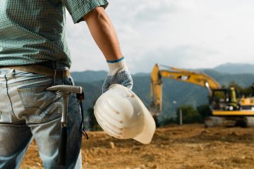 closeup back view of male engineer standing on construction site holding white hardhat